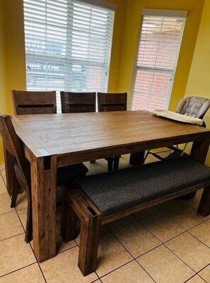 A wooden dining table with four chairs and a bench, set against yellow walls with windows. - Caleb’s King & Queen Home. 
Kids/Pet friendly, Family games, Piano. (Lubbock)