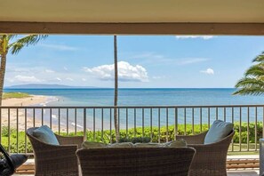 A balcony with wicker furniture and a view of the beach and ocean.