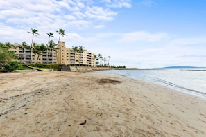 A beach with a hotel in the background, palm trees, and a clear sky.