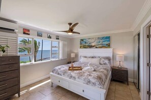 Une chambre à coucher comprenant un lit, un ventilateur de plafond, une fenêtre avec vue, une table de chevet et une commode.