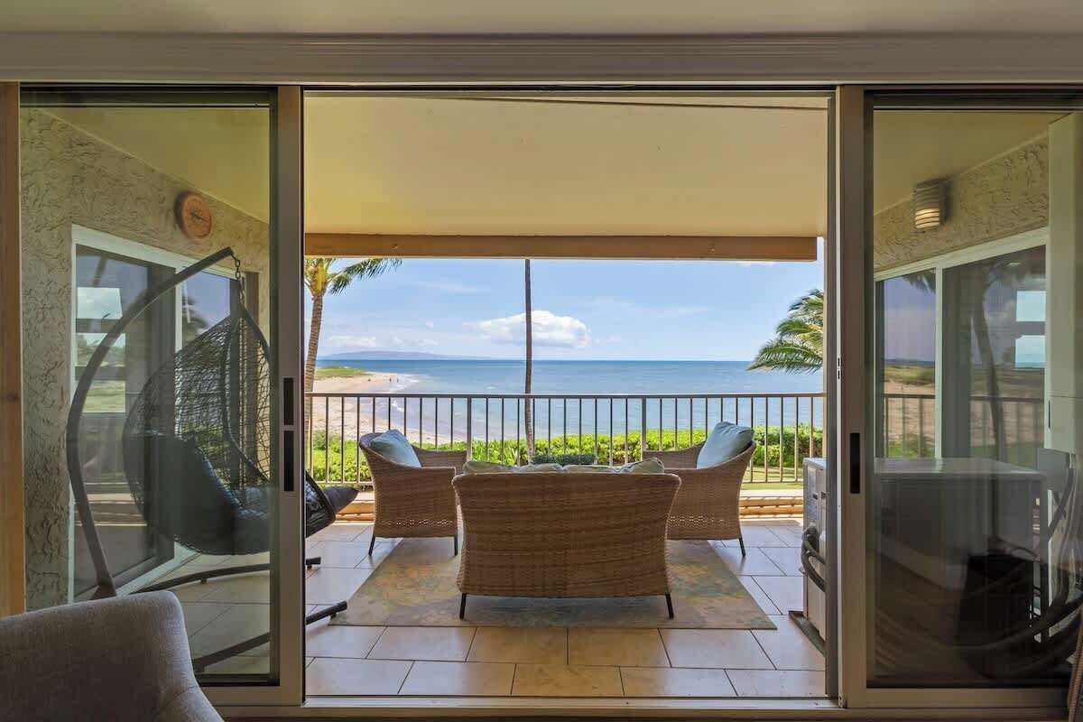 A balcony with wicker furniture, a glass door, and a view of the ocean.