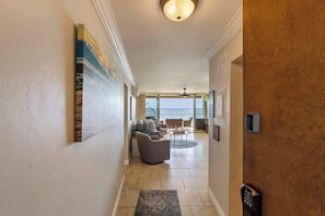 A hallway with a view to the outside, a seating area with a sofa and chairs, and a door with a keypad lock.
