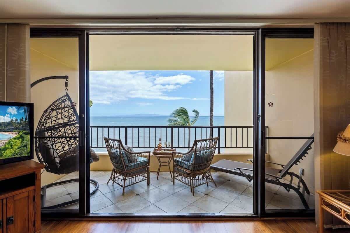Un balcon avec des fauteuils en osier, une table et un téléviseur posé sur un meuble en bois.