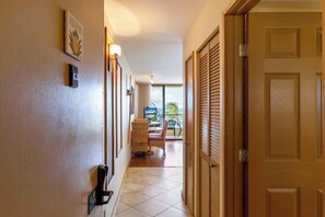 A hotel hallway with a wooden door, a wall-mounted light, and a view of the outdoor area.