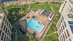 Una piscina en la azotea con vista a la playa, rodeada de palmeras y sillas de descanso.