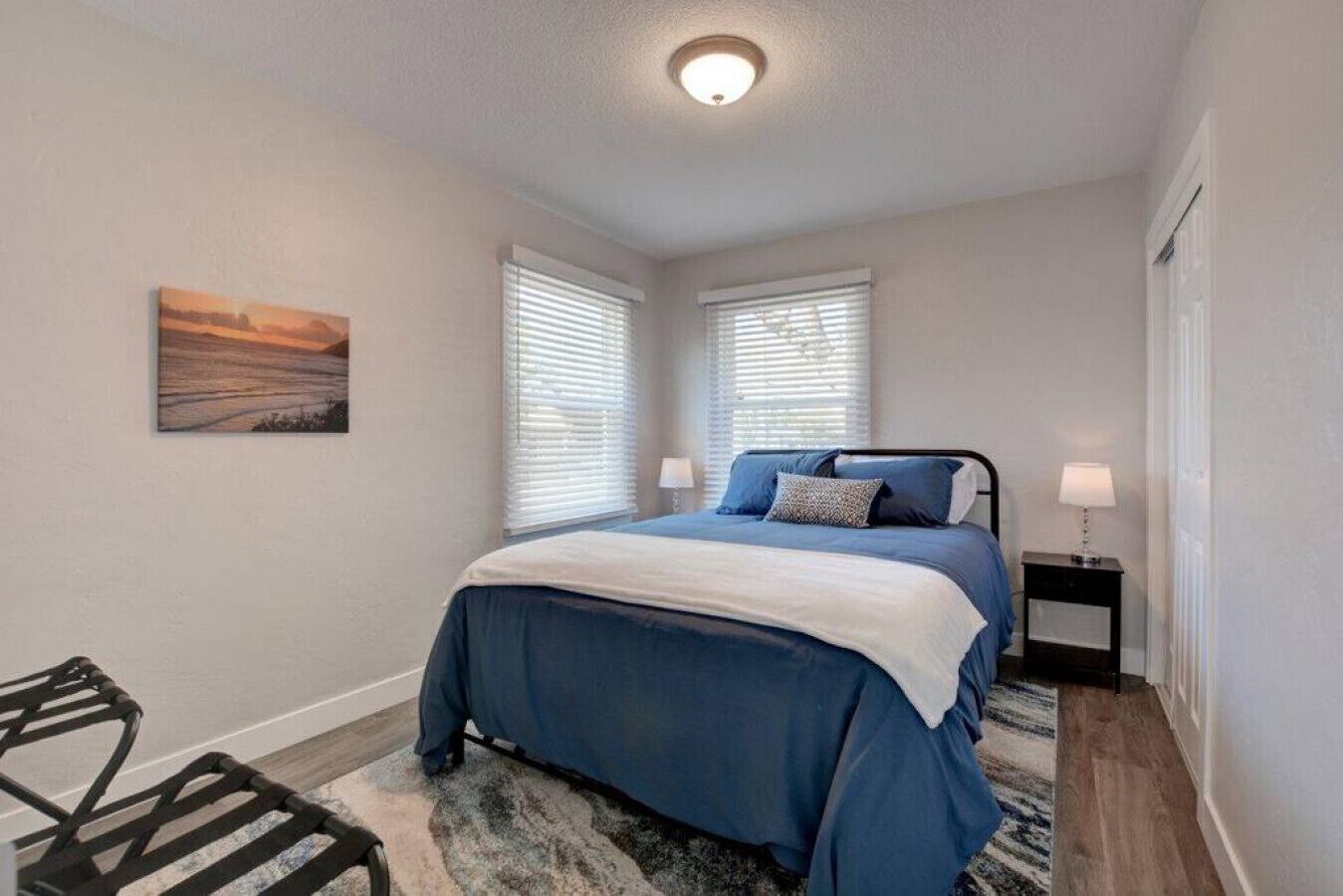 Une chambre à coucher avec un lit, deux tables de chevet, une chaise et un tableau accroché au mur.