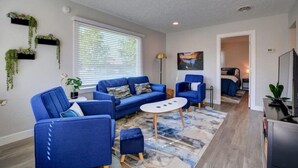 A modern living room with a blue sofa set, a coffee table, and a TV. There are plants on the walls and a painting on the wall. - Renovated Home in Central Point (Central Point)