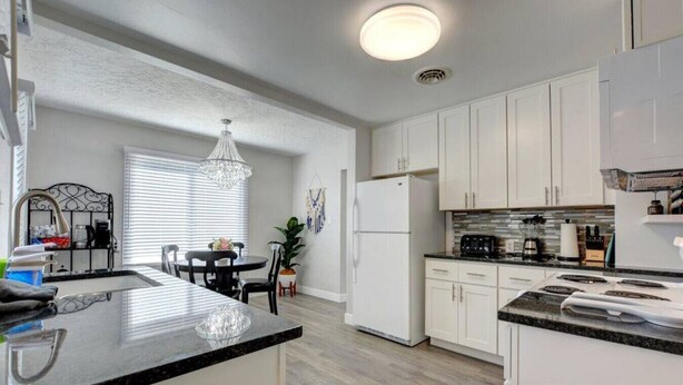 A modern kitchen with white cabinets, a granite countertop, and a dining area with a chandelier. - Renovated Home in Central Point (Central Point)