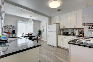 A modern kitchen with white cabinets, a granite countertop, and a dining area with a chandelier.