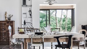 A dining area with a wooden table, chairs, and a view of trees through a large window.