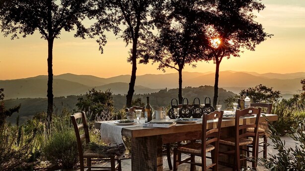 An outdoor dining table set with chairs, surrounded by trees and a scenic view of distant hills.