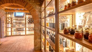 A wine cellar with wooden shelves and stone walls, containing various bottles and jars. - Villa Annabelle - Six Bedroom Villa, Sleeps 18 (Lucca)