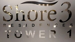 Un mur sur lequel on peut lire « Shore 3 Residences Tower 1 », avec un motif stylisé représentant une vague au-dessus du texte.
