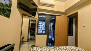 Une chambre à coucher comprenant un lit, une télévision, un climatiseur, une armoire et une porte donnant sur un balcon.