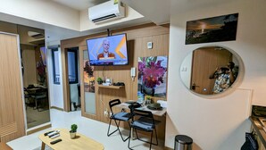 Un espacio de oficina moderno con un televisor montado en la pared, un espejo redondo y una zona de comedor con sillas y una mesa.