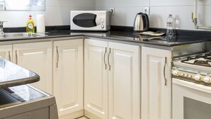 Una cocina con armarios blancos, microondas, hervidor y estufa.