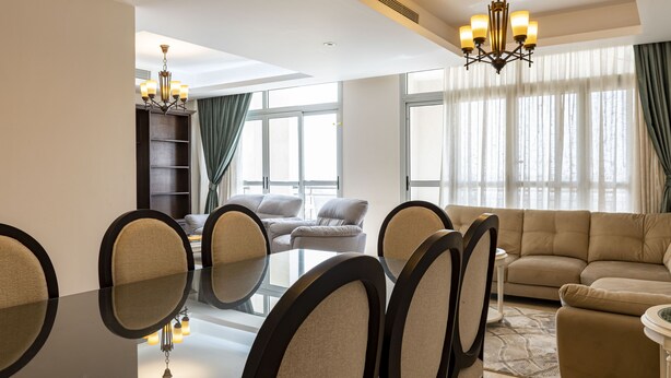 Una sala de estar moderna con una mesa de comedor de vidrio, sofás beige y un candelabro.