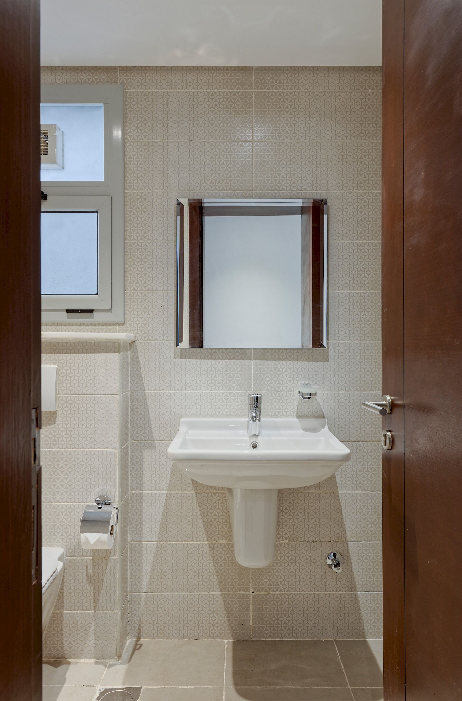 A bathroom with a white sink, a mirror, and patterned tiles.