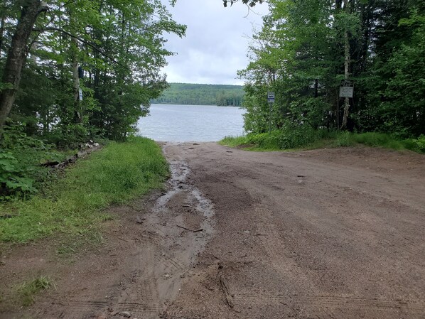 Un sentier de terre mène à un lac bordé d’une forêt dense.