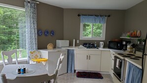 A compact kitchen with white cabinets, a dining table with chairs, a microwave, and a stove. - BIRCH HAVEN (Bancroft)
