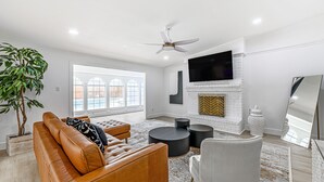 Una sala de estar moderna con un sofá de cuero, mesas redondas negras, un sillón blanco, una chimenea y un televisor grande montado en la pared.