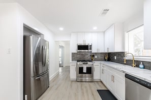 Una cocina moderna con electrodomésticos de acero inoxidable, armarios blancos y salpicadero negro.