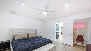 Un dormitorio moderno con una cama, un banco, un ventilador de techo y un letrero de neón.