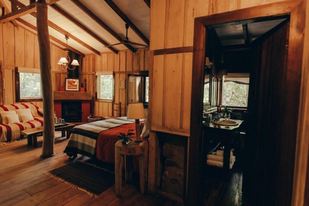 Une pièce chaleureuse aménagée dans un chalet en rondins, avec un lit, une cheminée, une petite table et une fenêtre.