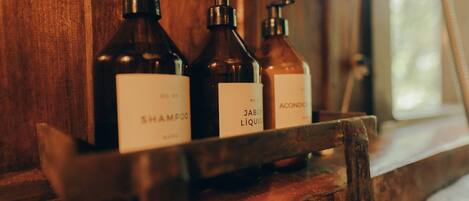 Three bottles of shampoo, a bottle of liquid soap, and a bottle of hand sanitizer on a wooden shelf.