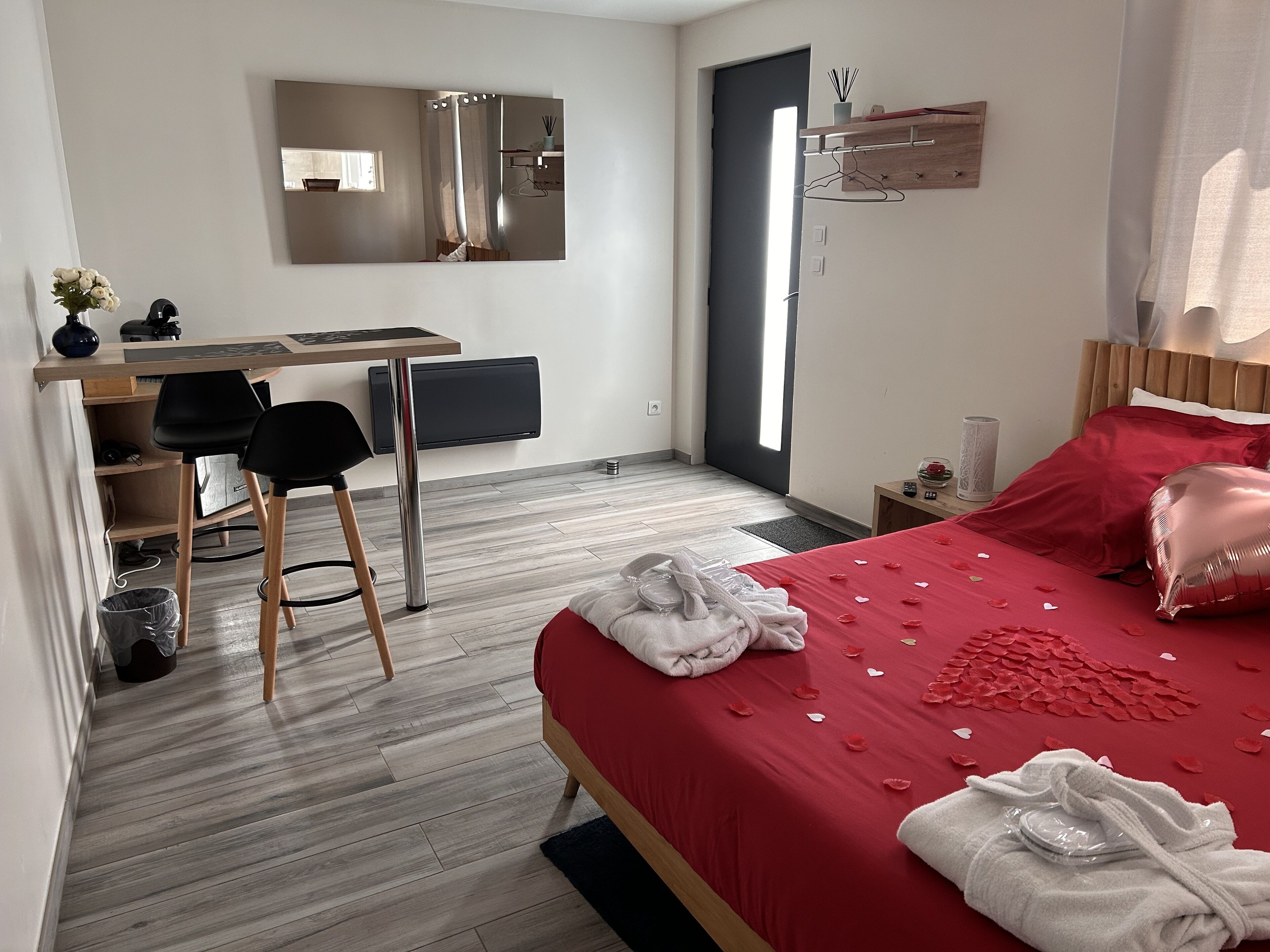 A modern bedroom with a red bedspread, a wooden desk, a chair, and a large mirror.