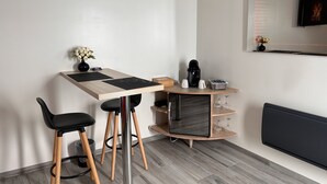 Un espacio de trabajo moderno y funcional, con un escritorio de madera, dos sillas negras, una cafetera y una pequeña estantería con adornos.