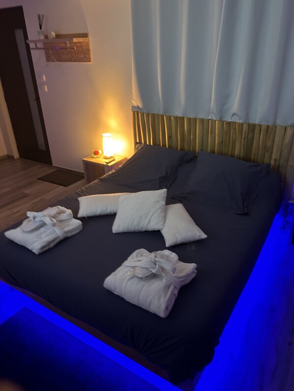 Una cama bien hecha con almohadas y toallas, una mesita de noche con lámpara y un cabecero de madera.