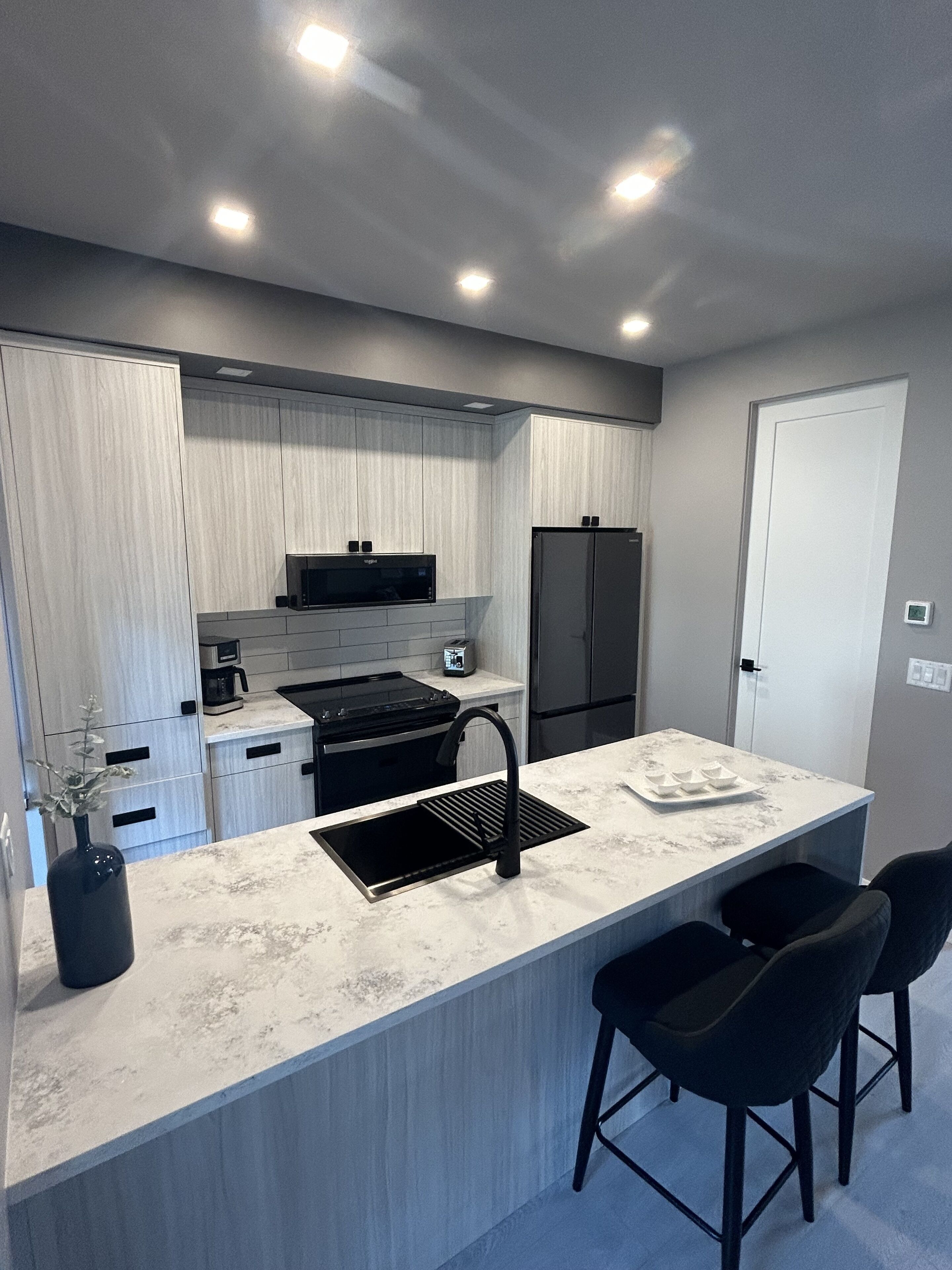 Una cocina moderna con una isla central, electrodomésticos negros y una puerta blanca.