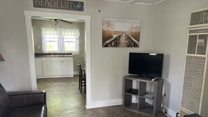 Un salon avec un téléviseur posé sur un meuble, un canapé et un coin repas avec une cuisine en arrière-plan.