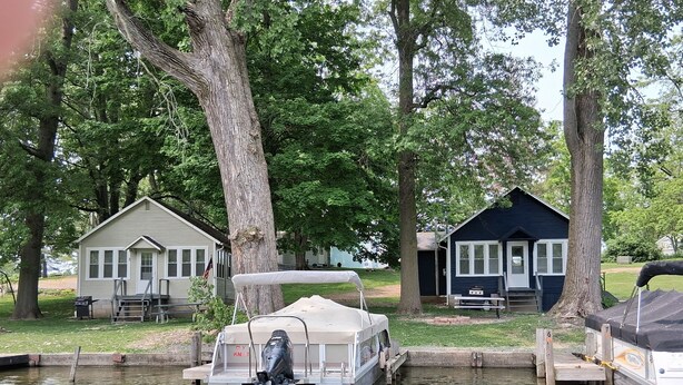 Un bateau à moteur était amarré à un quai en bois, doté d’un espace de repos abrité, et était entouré d’arbres et de deux petites cabanes.