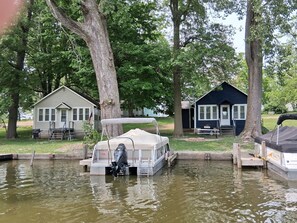 A motorboat docked at a wooden pier with a covered seating area, surrounded by trees and two small cabins. - Newland's Resort: Cozy Channel Front Cottage #2 on Indian Lake with a boat dock (Lakeview)
