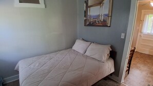Une chambre à coucher avec un lit, un tableau accroché au mur et une porte donnant sur une autre pièce.