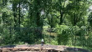 A stone patio with a birdbath and a fence in a wooded area. - Cozy Treehouse on Lake Conroe w/ large nest deck with a creek view (Willis)