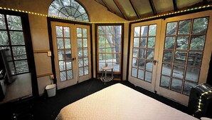 A bedroom with a large bed, multiple windows, and a view of the outdoors. - Cozy Treehouse on Lake Conroe w/ large nest deck with a creek view (Willis)