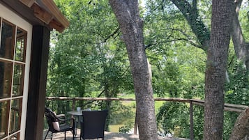 Une terrasse en bois avec une table et des chaises, donnant sur un étang et entourée d’arbres.