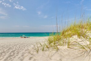 Een strand met duinen en een helderblauwe lucht.