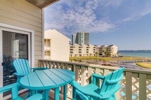 Ein Balkon mit türkisfarbenen Stühlen und einem Tisch, mit Blick auf einen Hafen und hohe Gebäude.