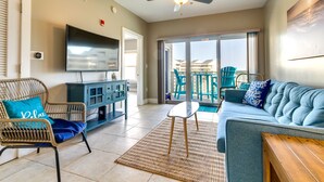 A living room with a sofa, a chair, a television, and a ceiling fan. - Bayfront Pensacola Beach Condo w/ Pool & Elevator (Pensacola Beach)