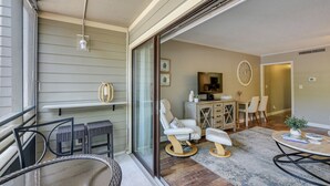 A modern living room with a glass door leading to a balcony, a television, and a dining area with chairs and a table. - Serene Myrtle Beach Condo w/ Resort Amenities! (Myrtle Beach)