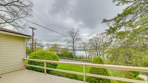 A wooden deck with a railing, overlooking a green lawn and a road. - Charming Canandaigua Lake House w/ Deck & Views! (Canandaigua)