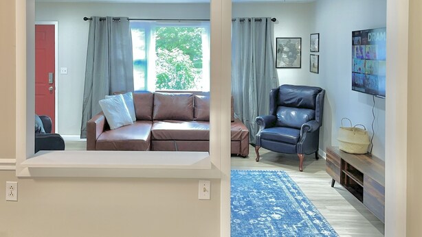 A living room with a brown sofa, a blue armchair, a blue rug, and a TV mounted on the wall. - Red Tail Cottage: Full Fence, Hammock Chair, Walk to Bass Pro, Movie Night (Springfield)