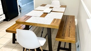 A dining table with a white chair, a bench, and a black refrigerator in the background. - Red Tail Cottage: Full Fence, Hammock Chair, Walk to Bass Pro, Movie Night (Springfield)
