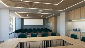Une salle de conférence dotée d’une grande table, de rangées de chaises, d’un écran de projection et d’un plafond en bois avec des spots encastrés.