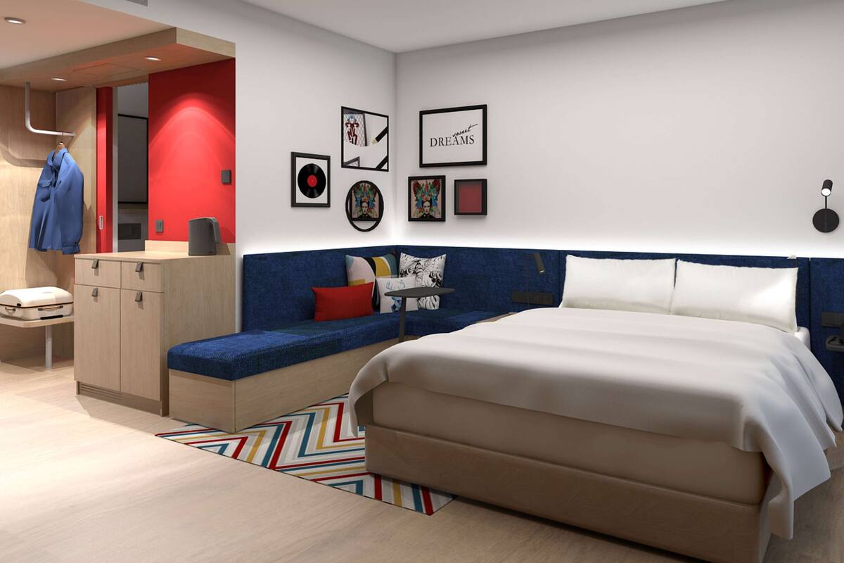 Ett modernt hotellrum med en stor säng, en sittgrupp med soffa och kuddar, ett skrivbord med stol och en garderob.