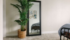 Una habitación con un espejo grande que refleja una cama, una cuna, una planta en maceta y cuadros en la pared.